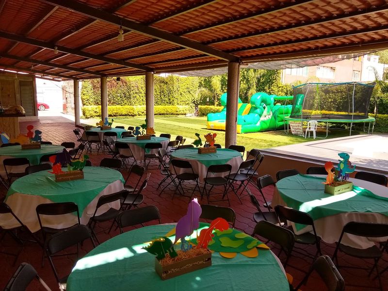 Mesas con mantel verde bajo el techado y el jardín al fondo